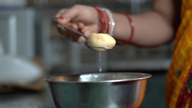 Close Up of Juicy Bengali Rosogolla on a Spoon with Liquid Sugar Dripping. Traditional Indian Sweet Rasgulla Held on Spoon in a Kitchen Setting.