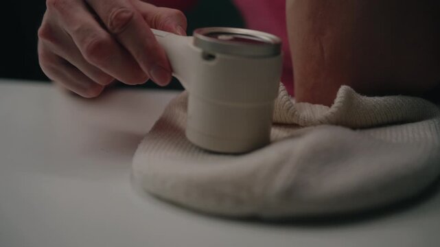 Close-up hands of unrecognizable man using modern electric lint remover machine on fabric garment, cleaning pilling and fuzz from cloth to refresh appearance and prolong life. Shooting in slow motion.