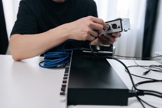 Person hands connecting audio interface to synthesizer or midi controller with xlr and jack cables, setting up home music studio for composing and recording sounds.