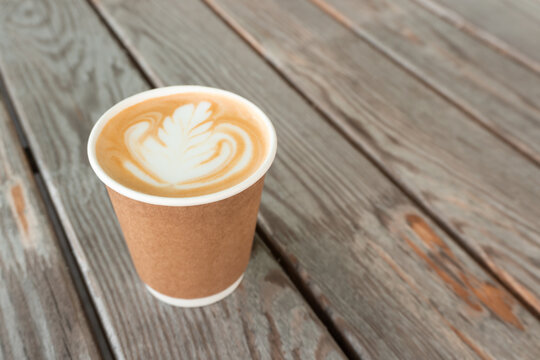 Cappuccino coffee with beautiful latte art in paper cup on wooden table background with copy space