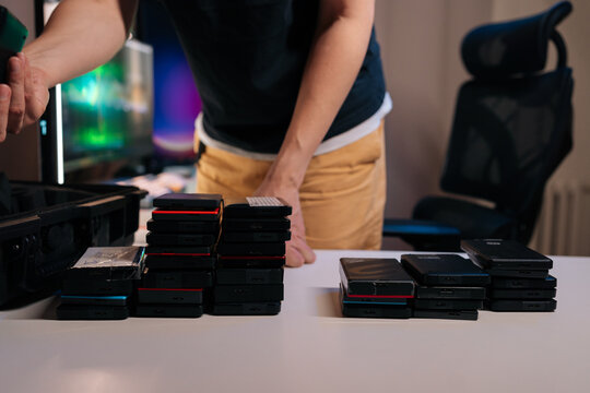 Man at desk organizes many external solid state drives. Stacks of devices for data storage backup sit on white table. Concept for technology, workflow, information management, digital security.