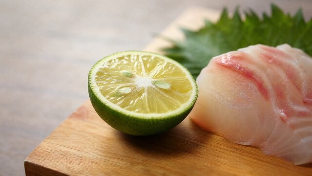 A halved sudachi fruit on a Japanese cutting board next to a piece of sashimi.
