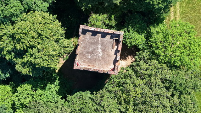 Historischer R&ouml;merturm inmitten eines dichten, gr&uuml;nen Waldst&uuml;cks, umgeben von weiten Feldern und Wiesen in einer idyllischen l&auml;ndlichen Landschaft aus der Vogelperspektive fotografiert.