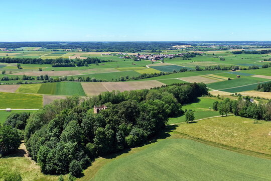 Historischer R&ouml;merturm inmitten eines dichten, gr&uuml;nen Waldst&uuml;cks, umgeben von weiten Feldern und Wiesen in einer idyllischen l&auml;ndlichen Landschaft aus der Vogelperspektive fotografiert.