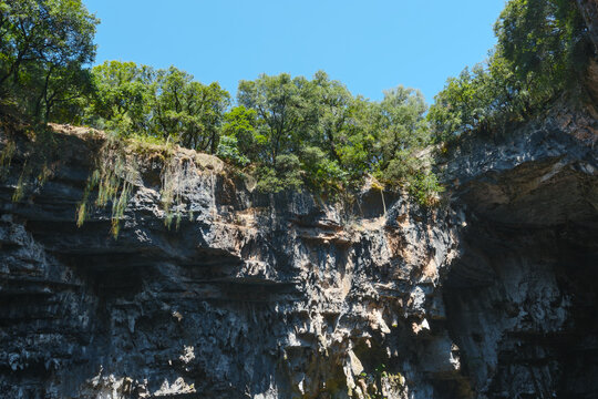 Rock formation with tree tops and clear sky, Melissani Lake