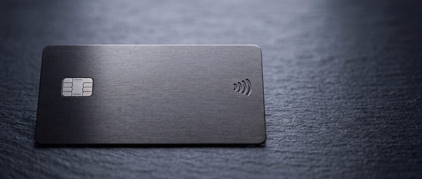 Sleek black metal credit card with chip and contactless symbol on dark slate surface