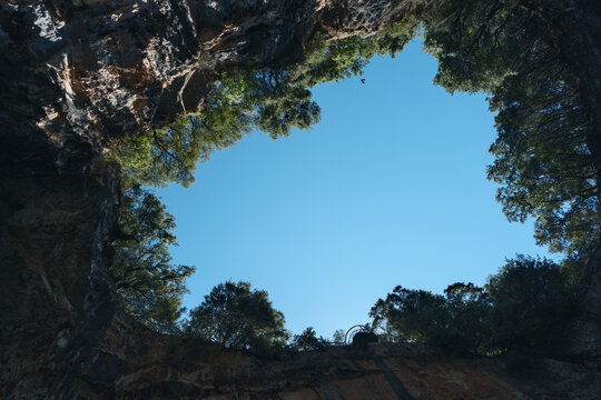 Cave entrance with blue sky and tree-covered rocky edges
