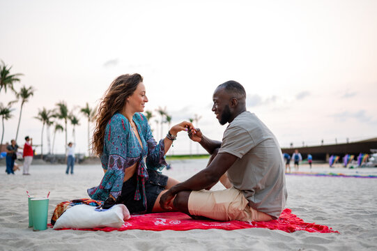 A romantic young couple enjoying a peaceful picnic on a sandy beach at sunset, intimate conversation
