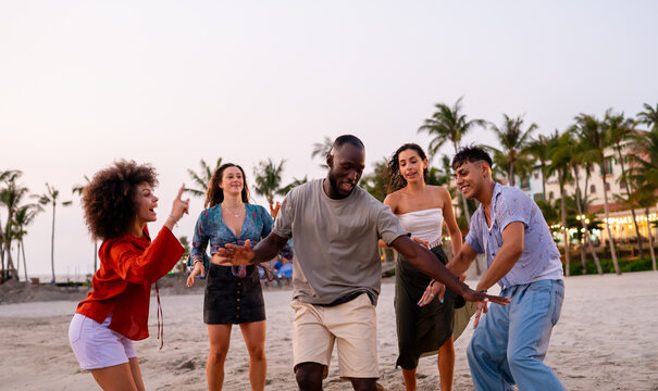 Happy young people embracing the beach lifestyle, dancing barefoot in the sand, celebrating freedom