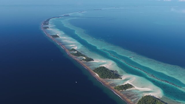 Aerial view of a long narrow atoll with lush green islands surrounded by turquoise coral reefs and deep blue ocean water in Kudahuvadhoo, Dhaalu Atoll, Maldives.