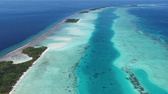Aerial view of a narrow tropical atoll featuring lush green islands and vibrant coral reefs surrounded by turquoise lagoons in Kudahuvadhoo, Dhaalu Atoll, Maldives.