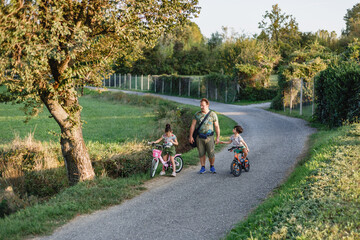 Naklejka premium Father Walking with Children Riding Bicycles on a Rural Country Road