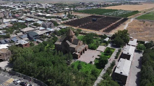 An aerial drone shot captures the historic Saint Gayane Church, an ancient Armenian apostolic church showcasing its beautiful stone architecture and green courtyard in the city of Vagharshapat.

