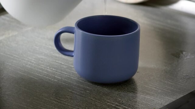 Close-up video of hot water being poured into a blue mug with tea, mint and lemon, creating a cozy scene of tea preparation, warmth and relaxation.