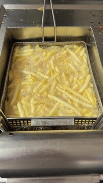 French fries frying in hot oil inside a deep fryer, golden crispy, bubbling fat, fast food cooking.