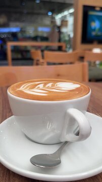 Cup of cappuccino in a cozy coffee shop, foam art, warm aroma, ceramic mug, casual morning break.