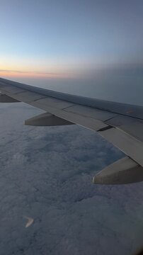 Passenger&rsquo;s view from airplane window flying above clouds after sunset, with vibrant colors in the sky and peaceful atmosphere surrounding the wing and horizon