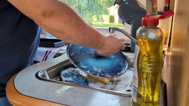 Man washing dishes in a motorhome kitchen with his dog looking on.