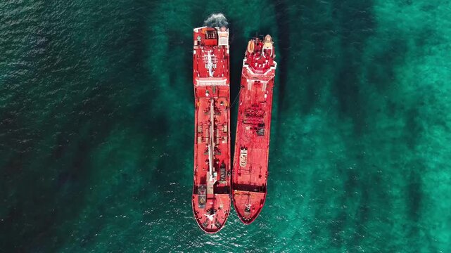 Aerial view of two red cargo ships side by side in the clear turquoise ocean water with dark shadows on the seabed in Nassau, New Providence, The Bahamas.