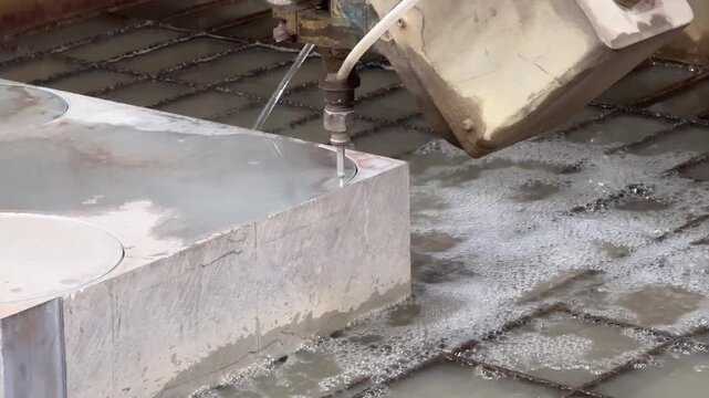 Waterjet cutting machine slices metal with high-pressure abrasive stream, producing precise edges amid water spray in an industrial workshop.