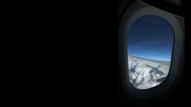 View from airplane window of white clouds over blue sky, soft peaks, sunlight, peaceful flight.