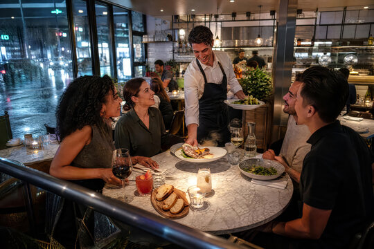 Bright Commercial Waiter Serving Dinner Plates To Guests In Busy Restaurant With Natural Restaurant Colors