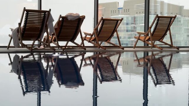 Row of loungers around pool before panoramic window overlooking metropolis, urban luxury meets serene water.