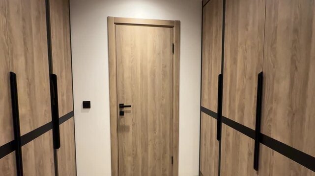 Panorama of a small walk-in closet with wooden cabinets, organized shelves, and warm interior lighting.