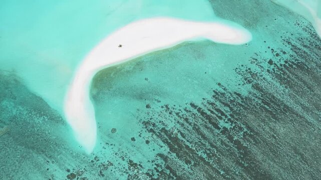 Aerial view of a crescent-shaped white sandbank surrounded by turquoise coral reef waters and dark seabed patterns in Kudahuvadhoo, Dhaalu Atoll, Maldives.