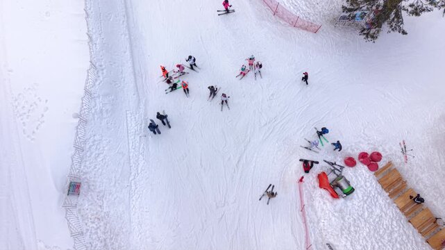 Aerial footage of a ski school lesson with beginner skiers practicing snowplow turns on a gentle slope at a mountain ski resort. The instructor leads the group downhill while other visitors enjoy wint