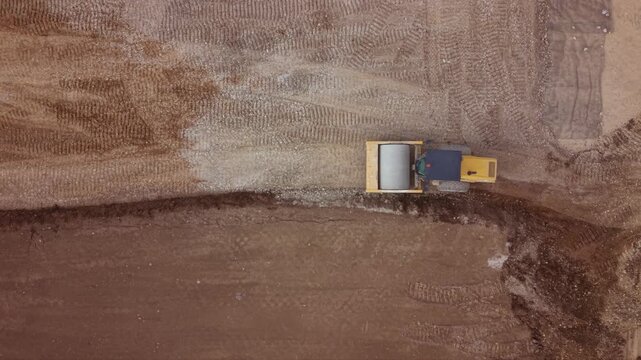 Aerial footage of a road roller compacting soil and aggregate during highway construction. The heavy compaction machine prepares the road base by compressing the ground, showcasing civil engineering, 