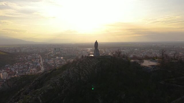 Aerial panoramic view of Alyosha Monument overlooking Plovdiv city at golden hour with sprawling urban skyline, Rhodope Mountains in the distance, historic landmark and dramatic evening clouds, Bulgar