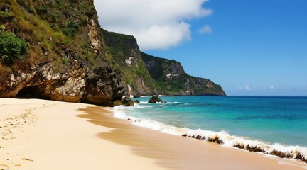 Naklejka premium Sandy beach meets turquoise ocean waves by tall green cliffside. Clear blue sky above calm water. Rocky island formations emerge from sea near tropical coast.
