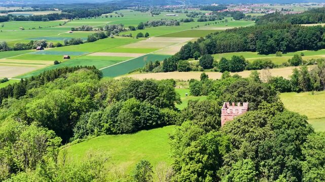 Historischer R&ouml;merturm inmitten eines dichten, gr&uuml;nen Waldst&uuml;cks, umgeben von weiten Feldern und Wiesen in einer idyllischen l&auml;ndlichen Landschaft aus der Vogelperspektive fotografiert.