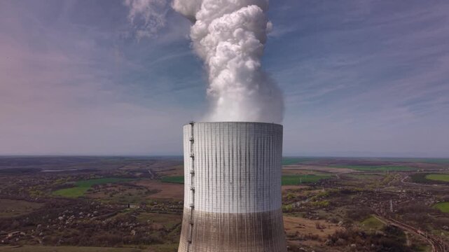 Close aerial footage of a massive cooling tower emitting dense white steam at an operating thermal power plant. The towering industrial structure dominates the landscape while showcasing electricity g
