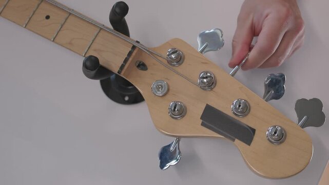 Male luthier performing stepwise electric guitar setup and stringing over workshop workbench