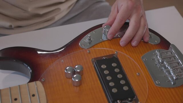 Hands assembling and wiring pickup on sunburst electric guitar through mid to late sequence