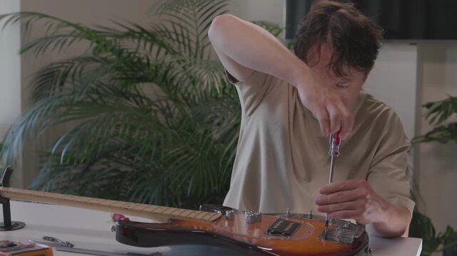 Hands assembling and wiring pickup on sunburst electric guitar through mid to late sequence