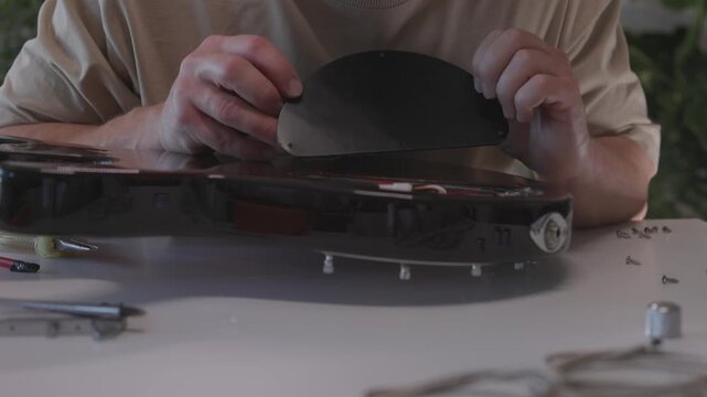 Male luthier performing stepwise electric guitar repair and testing in home workshop through