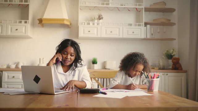 Housewife calling by mobile at home, portrait of woman and her child in kitchen. Motherhood and childhood, african american ethnicity, ordering goods by phone, call to delivery, little girl drawing