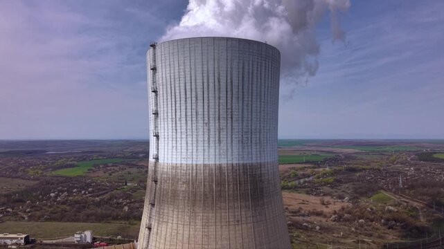 Close aerial footage of a massive cooling tower emitting dense white steam at an operating thermal power plant. The towering industrial structure dominates the landscape while showcasing electricity g