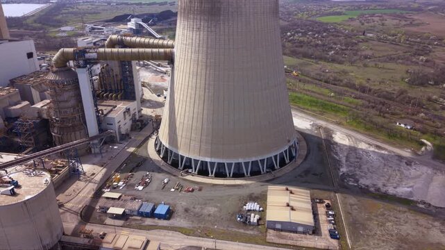 Close aerial footage of a massive cooling tower emitting dense white steam at an operating thermal power plant. The towering industrial structure dominates the landscape while showcasing electricity g