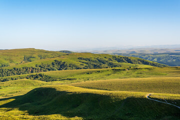 Obraz premium Layers of green mountains and hills in the haze during sunset. Panoramic View of Green hills and Meadow.