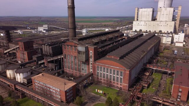 Aerial drone view of a large coal-fired power plant with towering smokestacks, turbine halls, conveyor systems, and industrial infrastructure. Wide overhead perspective of an electricity generation fa