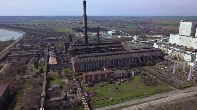 Aerial drone view of a large coal-fired power plant with towering smokestacks, turbine halls, conveyor systems, and industrial infrastructure. Wide overhead perspective of electricity generation.