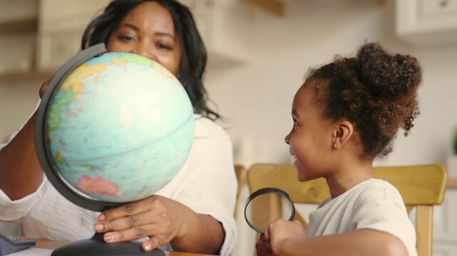 African american mom teaching her daughter at home, showing globe to girl. Geography lesson in school. Preschooler child enjoy fun geography lesson, education and homeschooling, exploring world