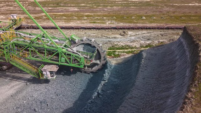 Close aerial view of a massive bucket wheel excavator operating in an open pit quarry, continuously excavating and transporting crushed rock via conveyor systems. Heavy mining equipment in action high