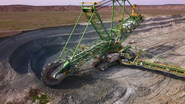Close aerial view of a massive bucket wheel excavator operating in an open pit quarry, continuously excavating and transporting crushed rock via conveyor systems. Heavy mining equipment in action high