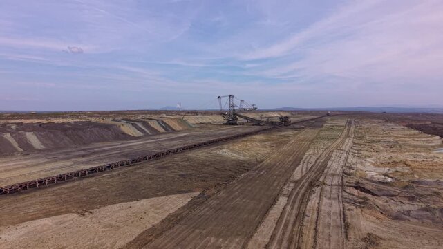 Aerial view of a long overland conveyor system transporting bulk material across a vast open-pit mining or industrial site, with transfer machinery, service roads and heavily disturbed terrain.