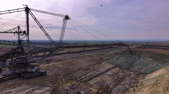 A large bucket-wheel excavator working in an open-pit mine, with conveyor structures, terraced earth, and a wide industrial landscape